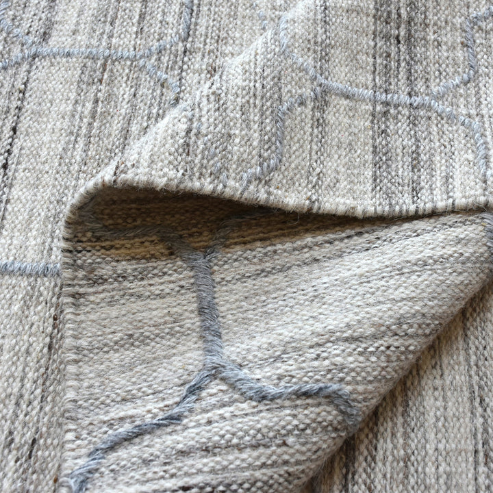 Bel handwoven wool and viscose rug with grey trellis lines on light grey, in a living room
