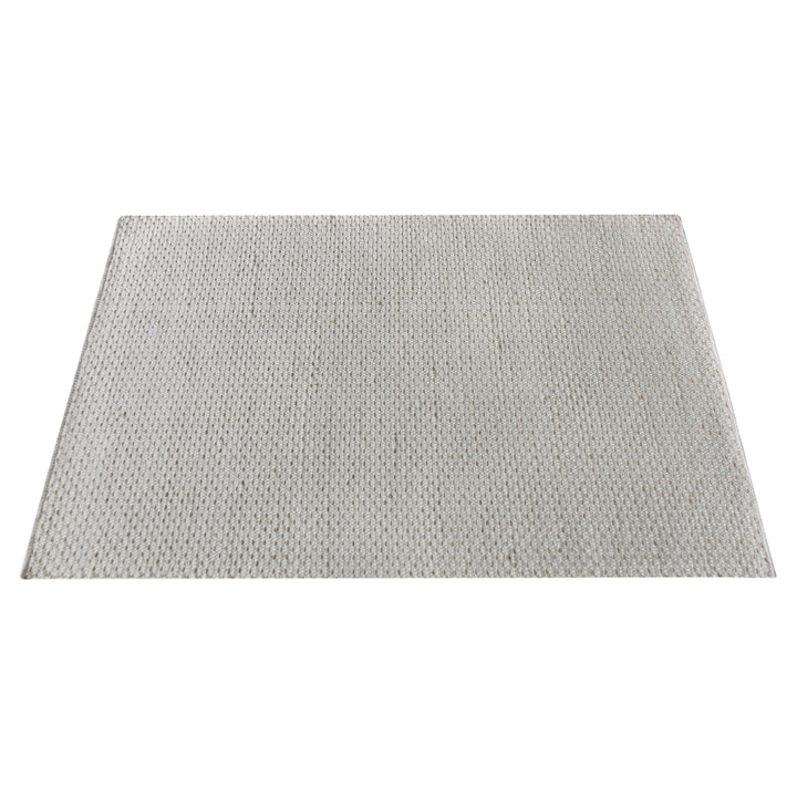 Kankar handwoven wool and jute rug in pale ivory-grey with a pebbled loop weave, in a bedroom