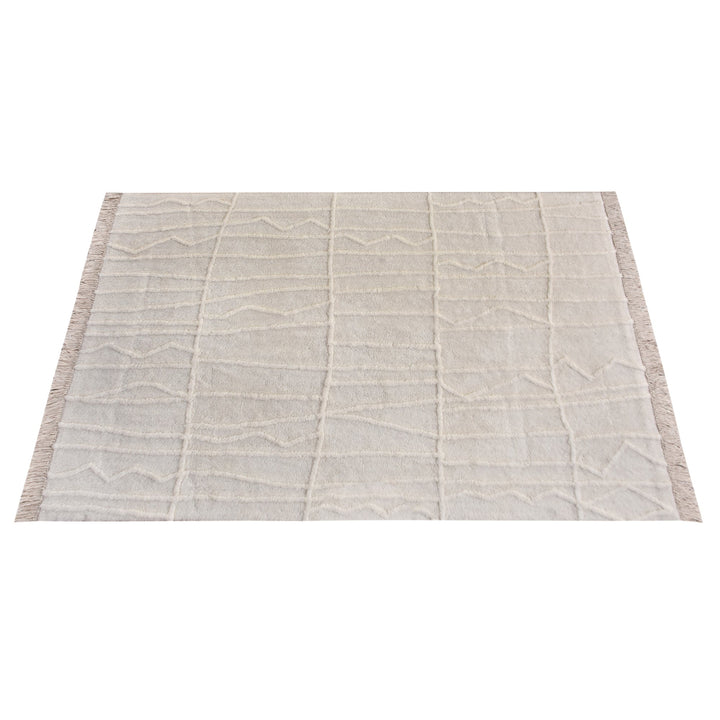 Swell tufted ivory New Zealand wool rug with carved waves and fringe, in a living room