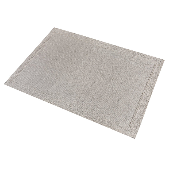 Linen handwoven wool rug in plain cream with a tonal border, in a bedroom