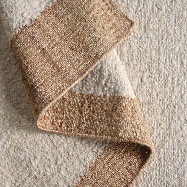 Kinari handwoven wool and jute rug in pale ivory with plain ribs and a tonal border, in a living room