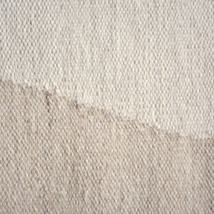 Kamaan handwoven wool flatweave rug with overlapping ivory and beige arcs, in a living room
