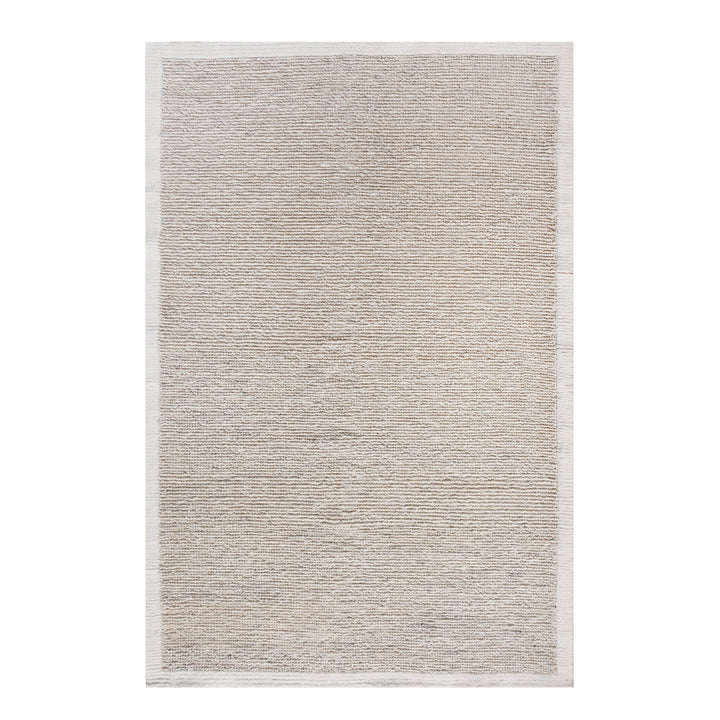 Shant handwoven flatweave wool rug in natural ivory with fine ribs and fringe, beside a bed