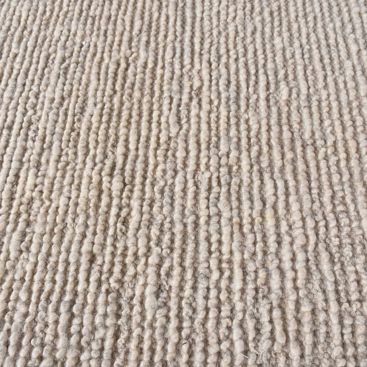 Shant handwoven flatweave wool rug in natural ivory with fine ribs and fringe, beside a bed