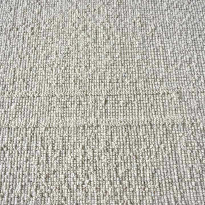Margin handwoven ivory wool rug with a raised tonal border, in a living room