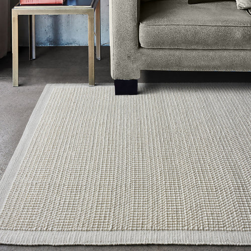 Basket handwoven cream wool rug with basketweave texture and tonal border, in a bedroom