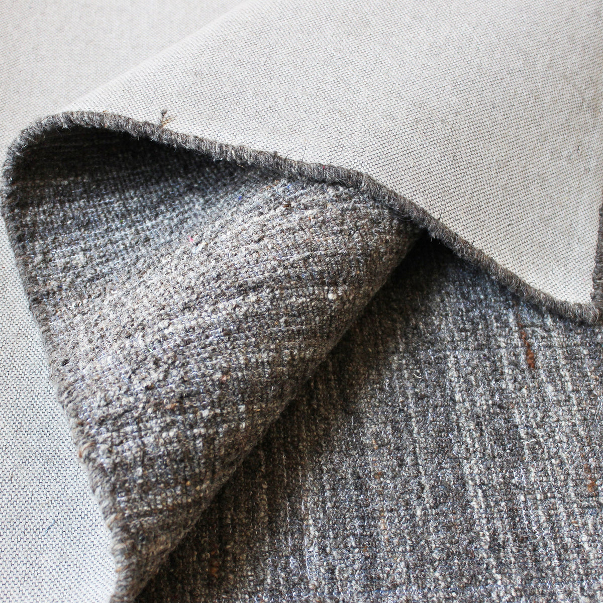 Saada handwoven flat wool rug in solid stone beige with charcoal, in a living room