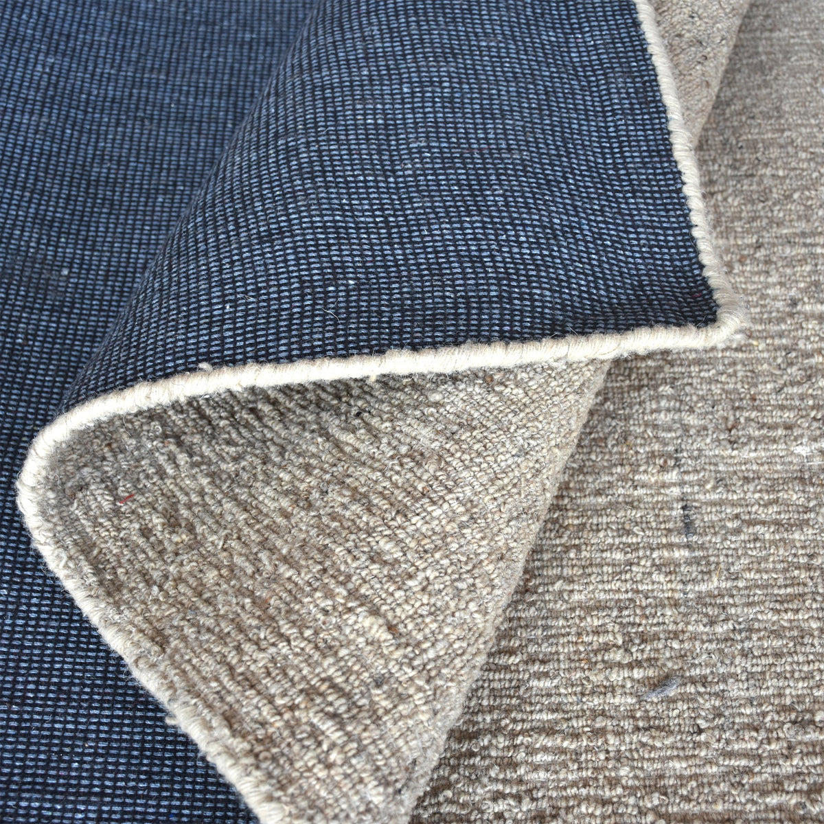 Saada handwoven flat wool rug in solid stone beige with charcoal, in a living room