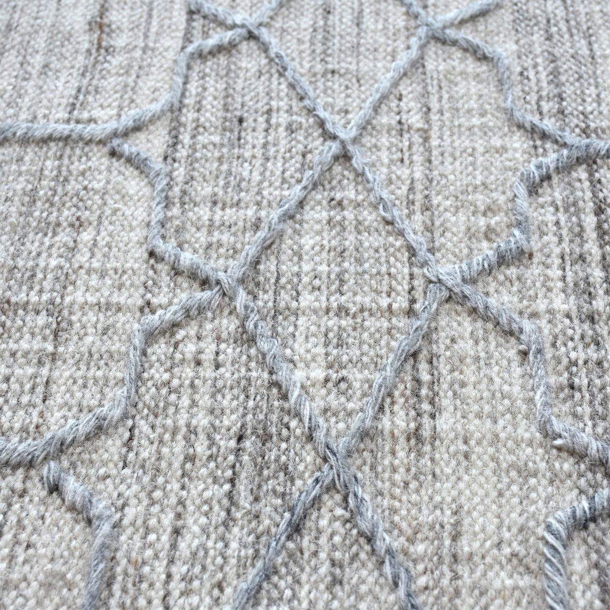 Bel handwoven wool and viscose rug with grey trellis lines on light grey, in a living room