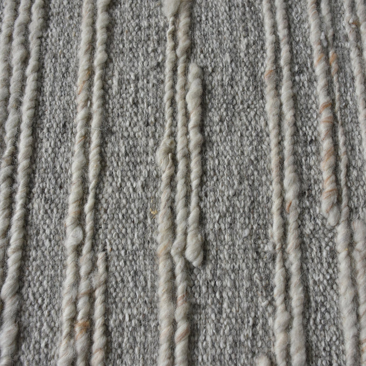 Surma hand-knotted wool rug in slate grey with raised ivory vertical stripes, in a living room