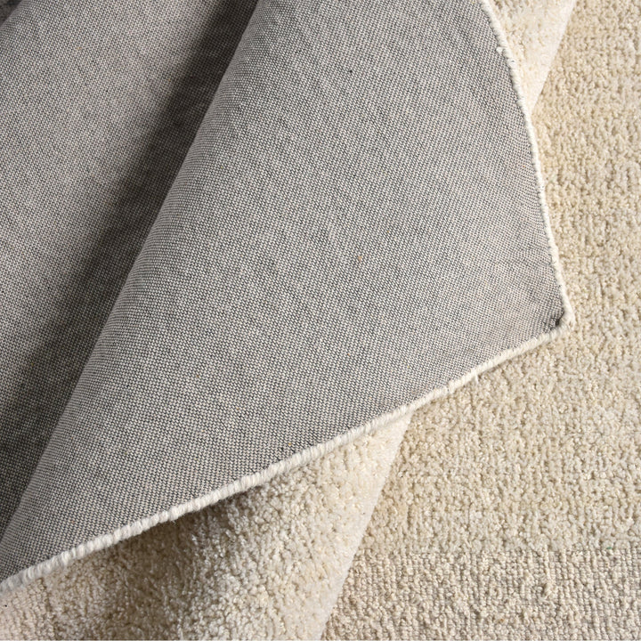 Gol handwoven wool rug in plain cream with a soft cut pile and a curved edge, in a nursery