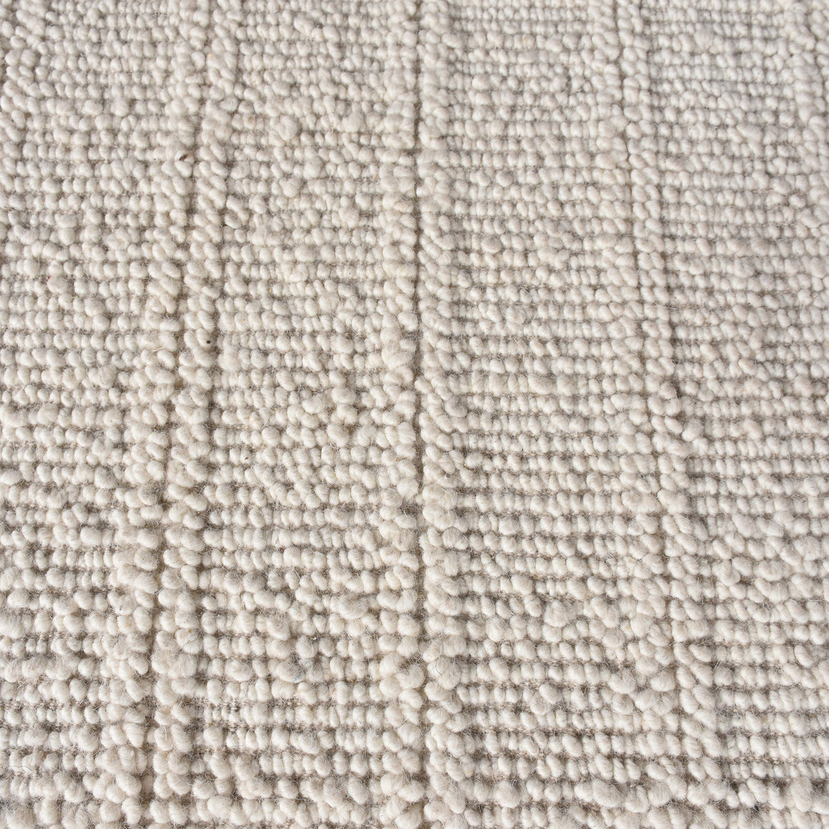 Oon handwoven ribbed wool rug in undyed oatmeal with horizontal ribs, under a coffee table