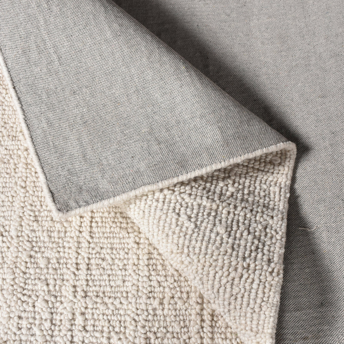 Oon handwoven ribbed wool rug in undyed oatmeal with horizontal ribs, under a coffee table