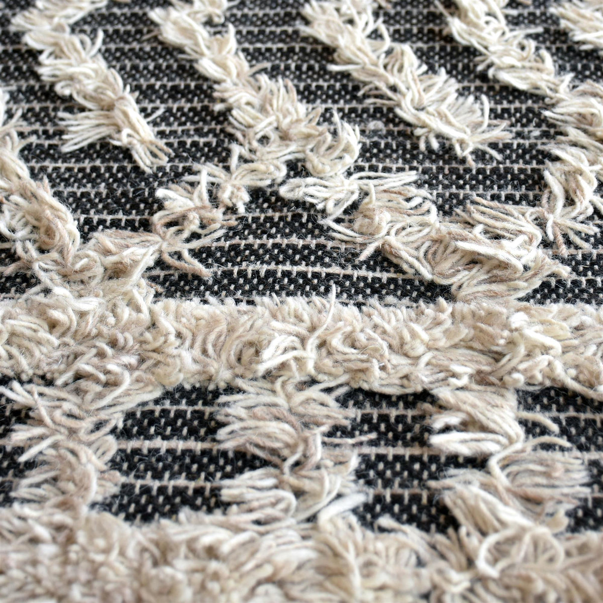 Tassel tufted wool rug with charcoal and ivory chevrons and shaggy bands, in a bedroom