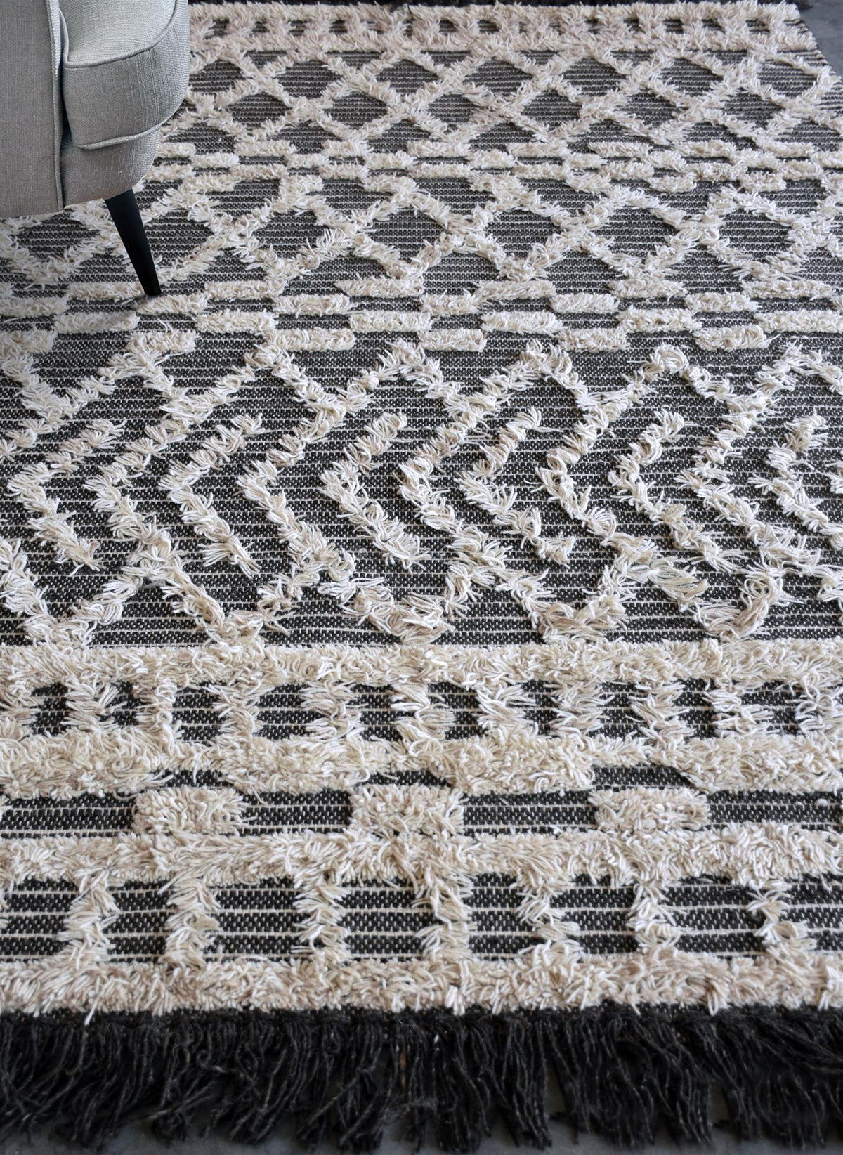 Tassel tufted wool rug with charcoal and ivory chevrons and shaggy bands, in a bedroom