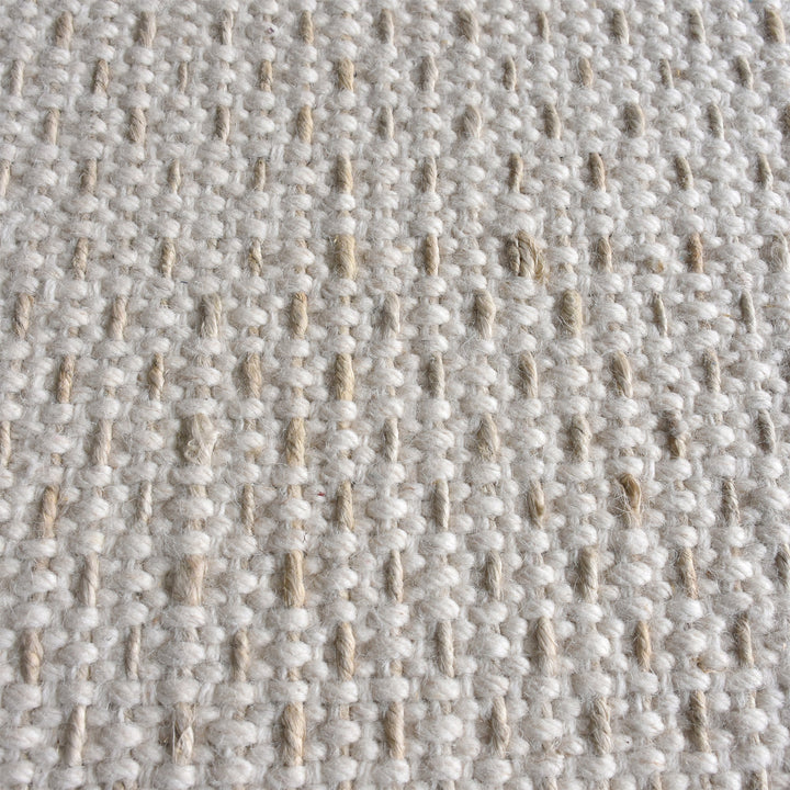 Kankar handwoven wool and jute rug in pale ivory-grey with a pebbled loop weave, in a bedroom