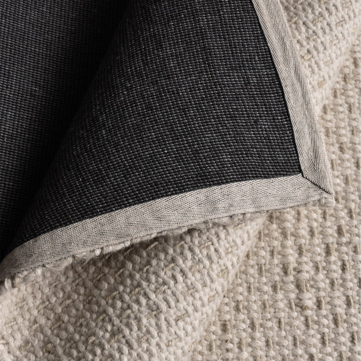 Kankar handwoven wool and jute rug in pale ivory-grey with a pebbled loop weave, in a bedroom