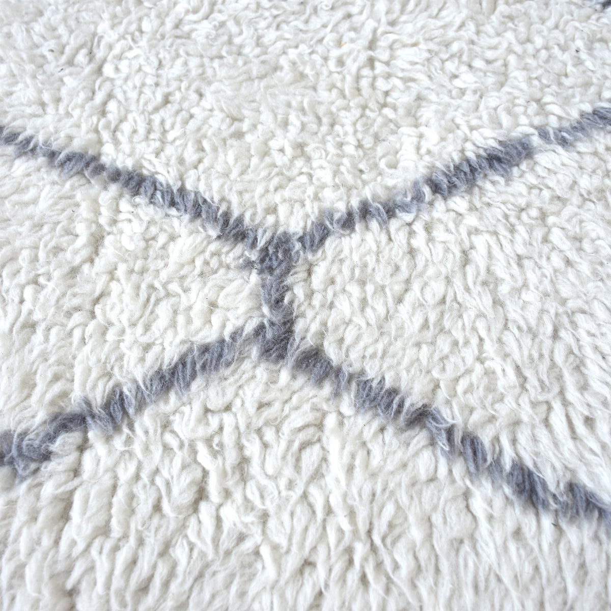 Kohra tufted New Zealand wool rug with a grey diamond lattice on white, in a living room