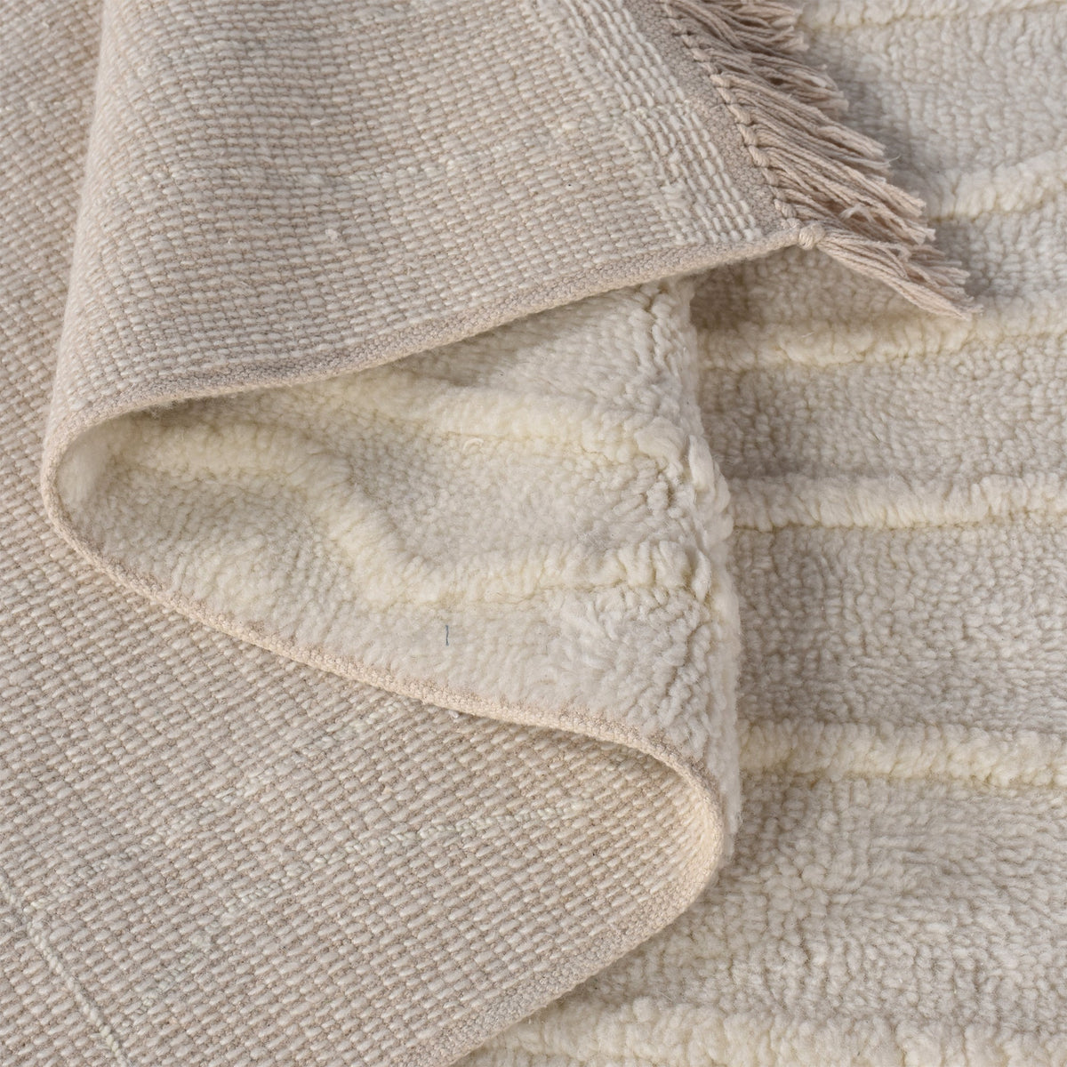 Swell tufted ivory New Zealand wool rug with carved waves and fringe, in a living room