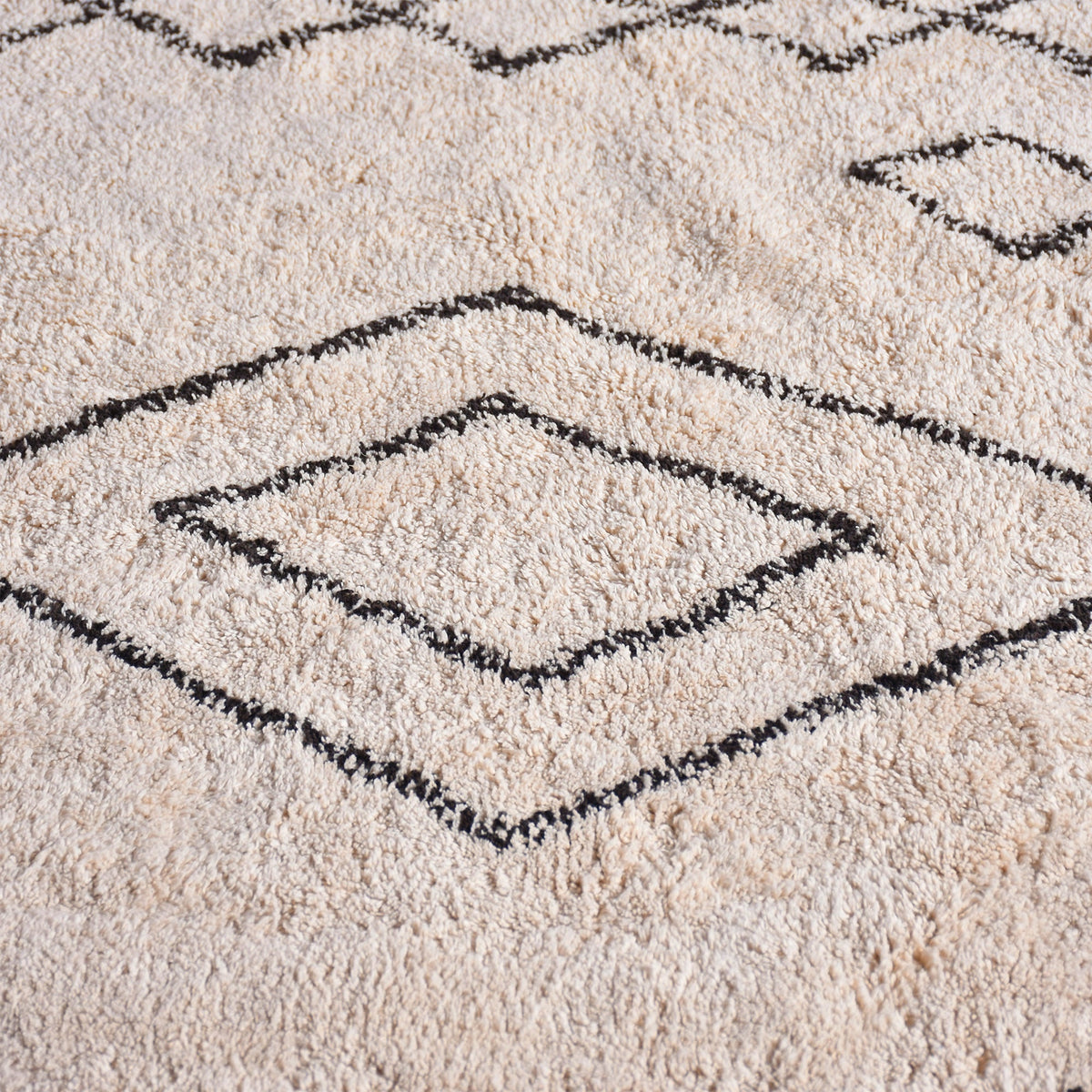Chhapa tufted cotton rug with black diamonds and chevron borders on bone white, in a study