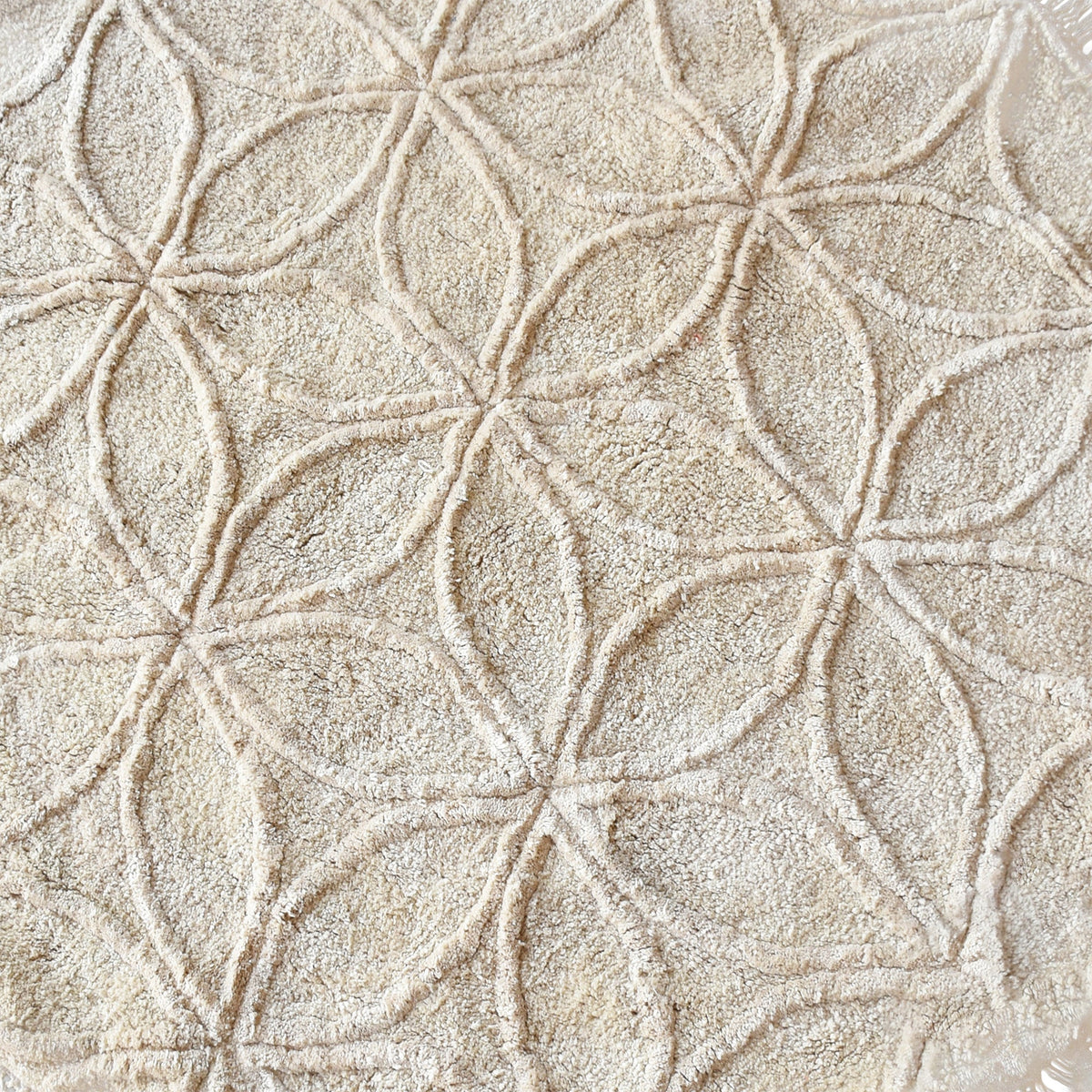 Phool round tufted cotton rug with a flower-of-life motif and fringe in raffia beige, in a bedroom