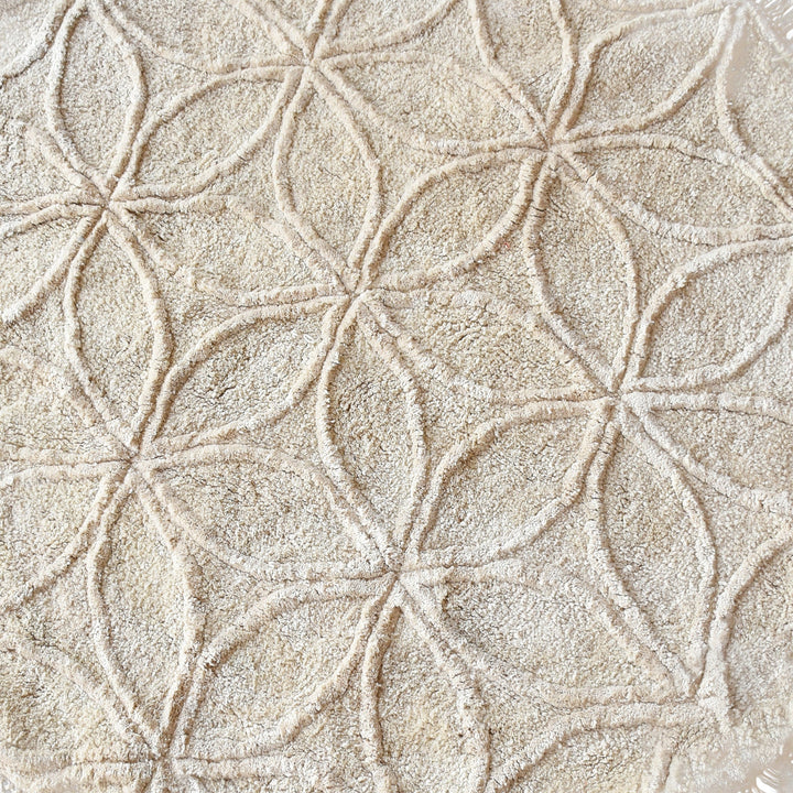 Phool round tufted cotton rug with a flower-of-life motif and fringe in raffia beige, in a bedroom
