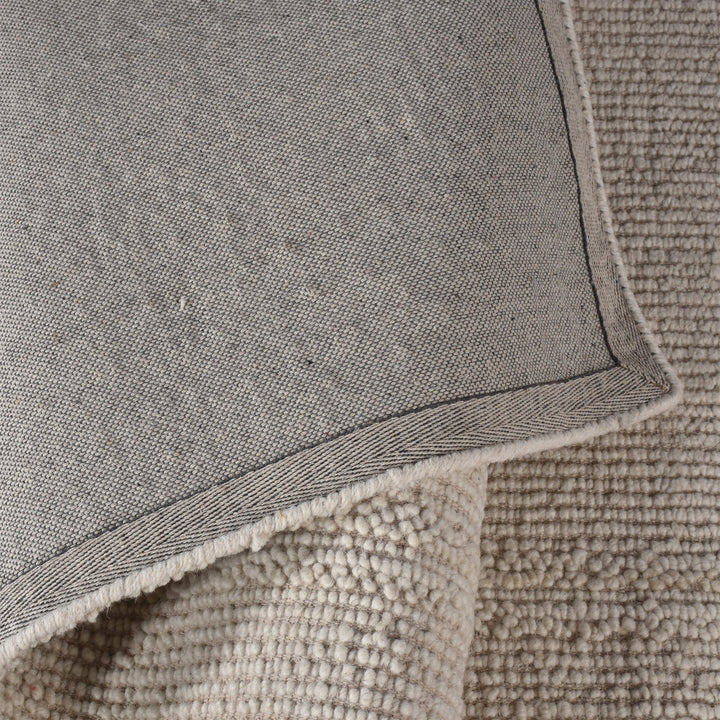 Linen handwoven wool rug in plain cream with a tonal border, in a bedroom