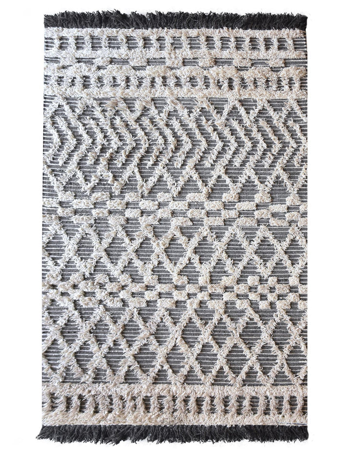 Tassel tufted wool rug with charcoal and ivory chevrons and shaggy bands, in a bedroom